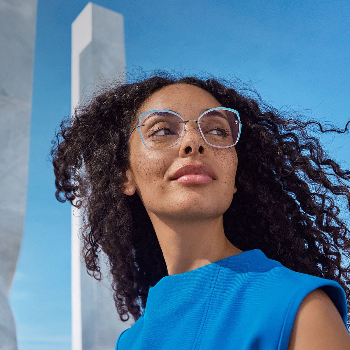 Frau mit dunklen Locken, Sommersprossen, blauem Oberteil und hellblauer Silhouette Brille TMA LaLignevon Optiker Gronde